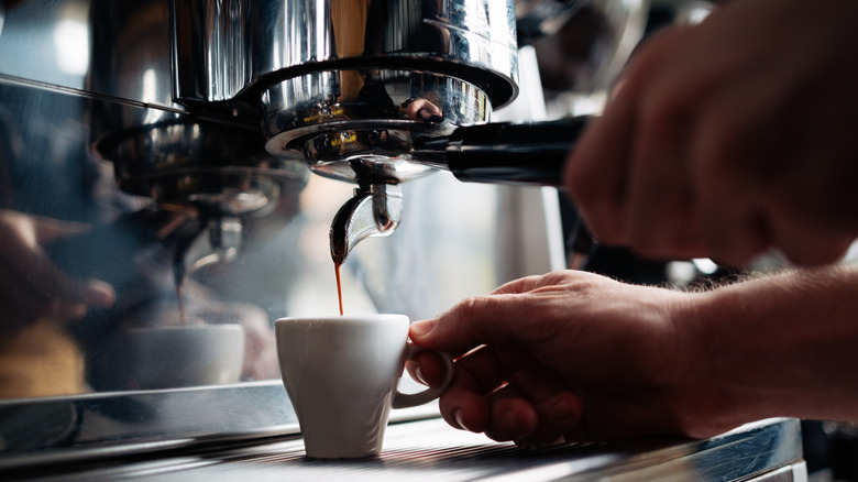 Mano vertiendo un trago de espresso en una taza de espresso blanca