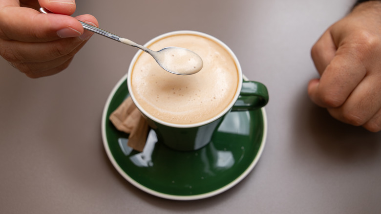 Cuchara sumergida en leche de microespuma de un café con leche en una taza verde