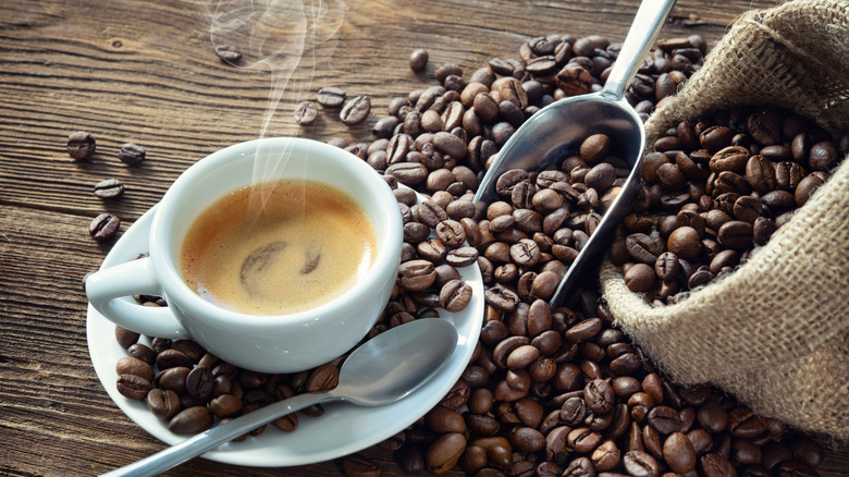 Taza de espresso humeante rodeada de granos de café derramados