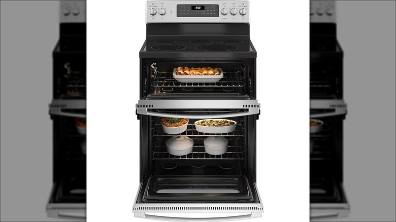 Vista abierta de la estufa eléctrica independiente GE de 30 pulgadas con tapa de vidrio y 5 quemadores con horno doble sobre un fondo blanco.
