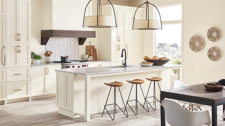Cocina moderna en color blanco cálido con luces colgantes de lino, taburetes de madera y hierro y cestas colgantes en la pared.