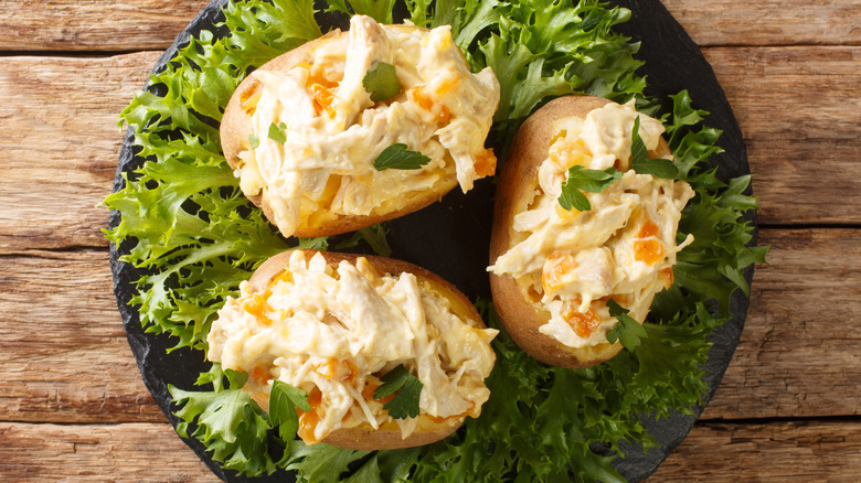 Patatas al horno con pollo de coronación sobre una cama de verduras en un plato negro