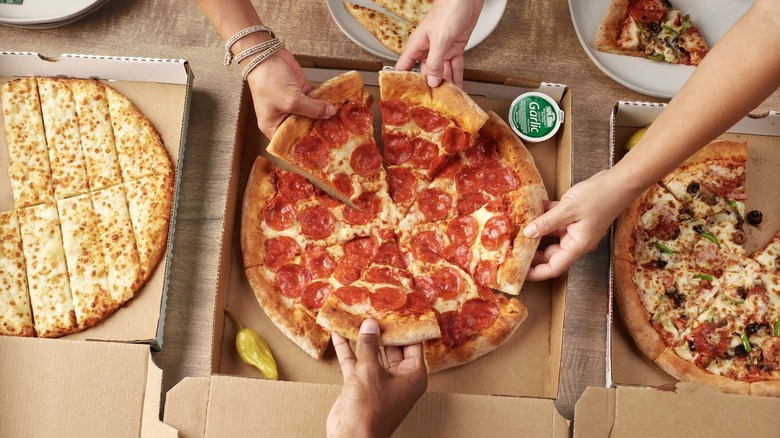 Cuatro manos tomando porciones de una pizza de pepperoni Papa Johns