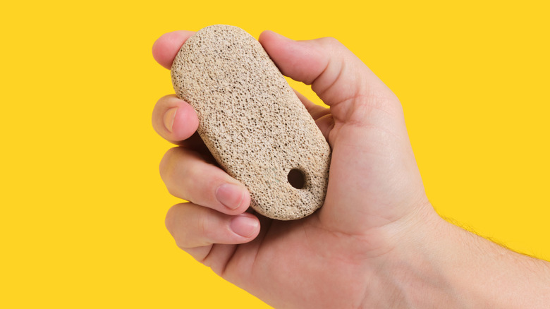 Mano sujetando piedra pómez sobre fondo amarillo