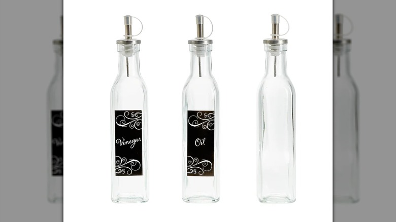 Tres botellas de aceite y vinagre de vidrio con boquillas metálicas sobre un fondo blanco.
