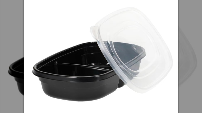 Porciones de comida negras de SureFresh Contenedor de plástico mediano para almacenamiento de alimentos con una tapa apoyada sobre un costado sobre un fondo blanco