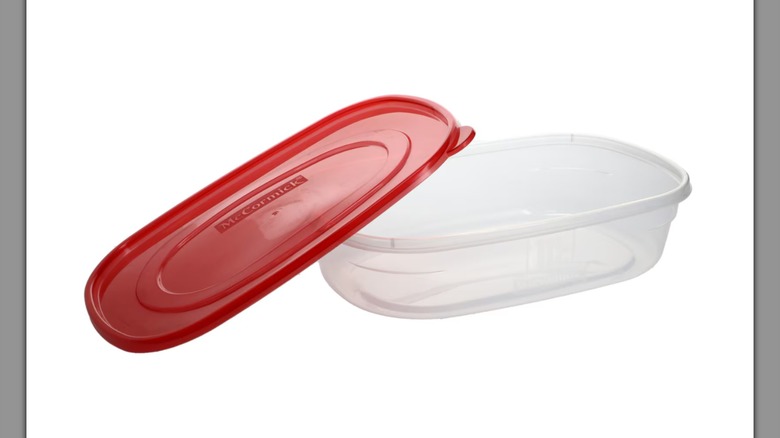 Un contenedor de almacenamiento rectangular McCormick con una tapa roja apoyada sobre un costado sobre un fondo blanco