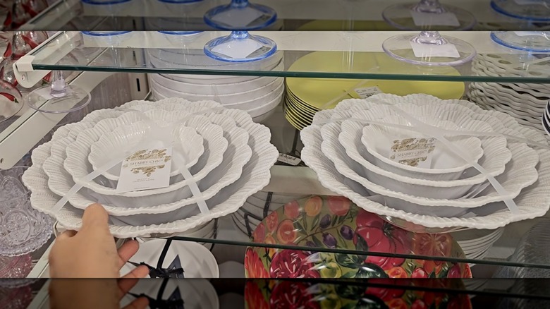 Una mano tocando un juego de cuatro tazones blancos con bordes festoneados en un estante de HomeGoods