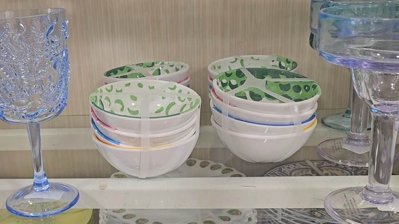 Cuatro juegos de cuatro tazones multicolores en un estante de HomeGoods junto a vasos azules