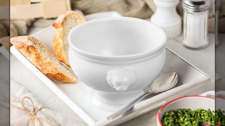 Un cuenco blanco con decoración de cabeza de león sobre una bandeja blanca con dos rebanadas de pan