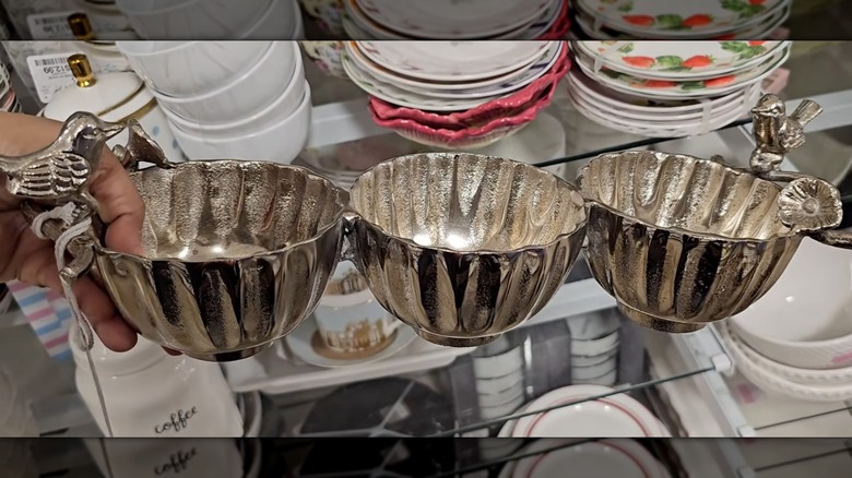 Una mano sosteniendo un recipiente de metal con decoración de pájaros en una tienda HomeGoods