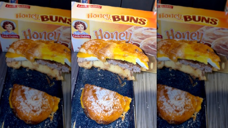 Una mano mostrando la sección transversal de un sándwich de desayuno Honey Bun frente a una caja de Little Debbie Honey Buns