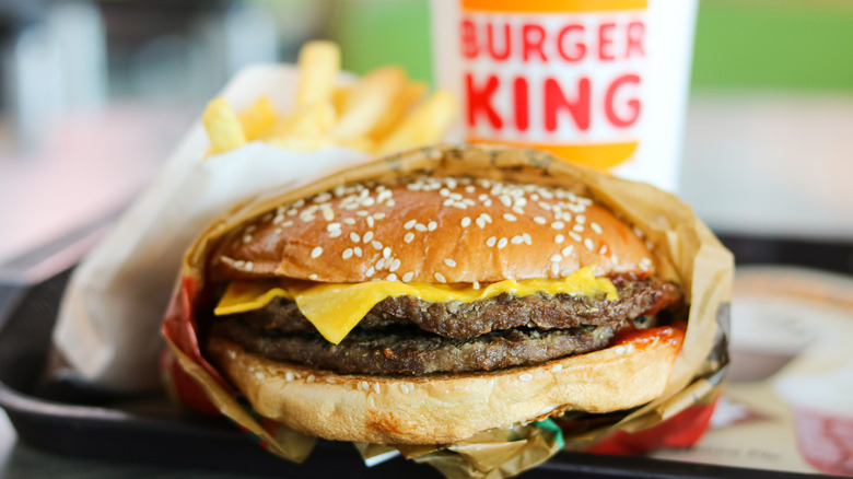 Una hamburguesa de Burger King con dos hamburguesas y queso delante de una taza de Burger King y papas fritas