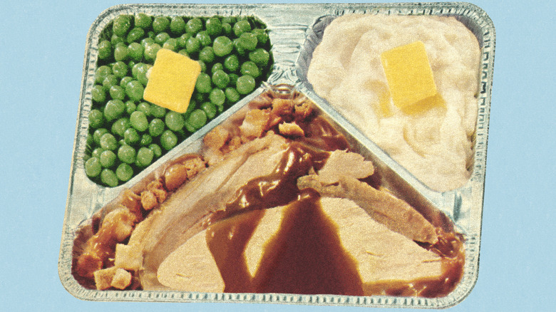 Una estilización vintage de pavo con salsa, relleno, guisantes y puré de patatas en una bandeja de aluminio
