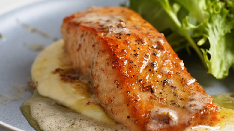 Un primer plano de un filete de salmón con un aderezo cremoso y picante en un plato junto a verduras
