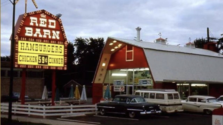 Exterior de una ubicación de Red Barn que muestra un estacionamiento y un letrero que anuncia hamburguesas y cenas de pollo.