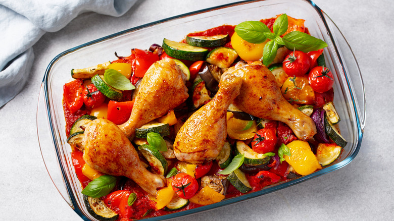 Un plato de vidrio lleno de muslos de pollo asado y verduras sobre una encimera