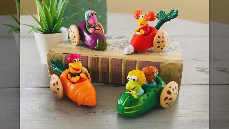 Cuatro juguetes de Fraggle Rock, dos de ellos en un libro con una maceta al lado