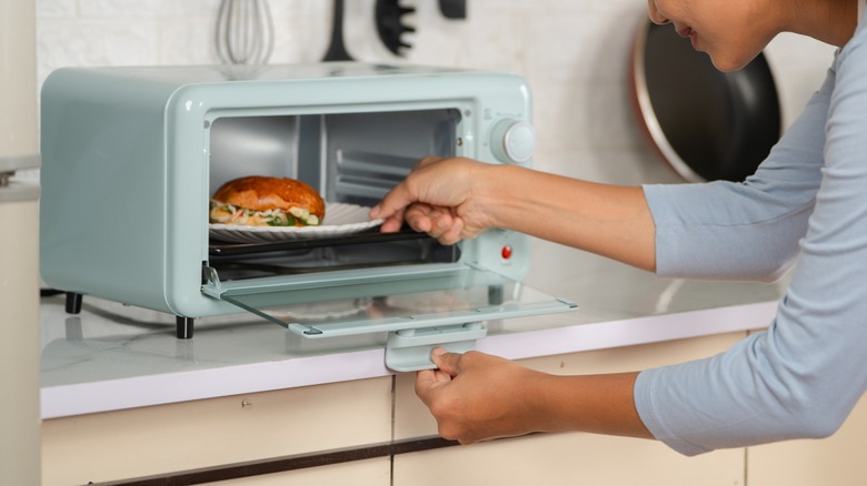Mujer cocinando comida en un horno tostador azul.