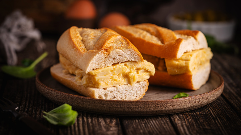 Dos mitades de un sándwich con tortilla española en un plato sobre una mesa de madera