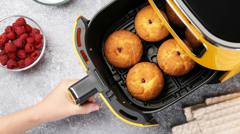 Una persona sacando el cajón de una freidora con muffins dentro.