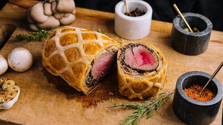 Beef Wellington sobre tabla de cortar con especias y champiñones