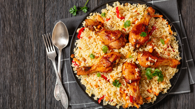Un plato de pollo pilaf con muslos de pollo encima junto a los cubiertos.