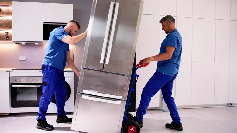 Dos tipos uniformados moviendo un refrigerador en una cocina