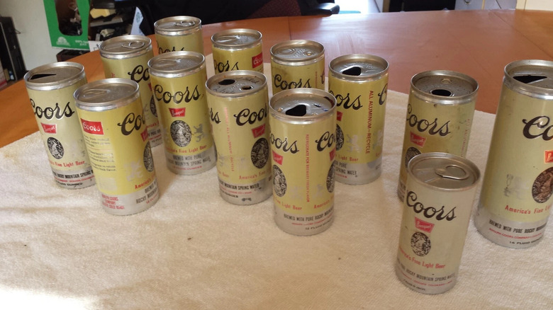 Lote de 13 latas de latas Coors antiguas con una mezcla de tapas abiertas y sin abrir sobre una mesa de madera