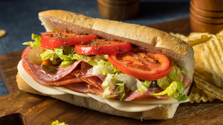 Un sub sándwich con carne, queso y ensalada junto a patatas fritas.