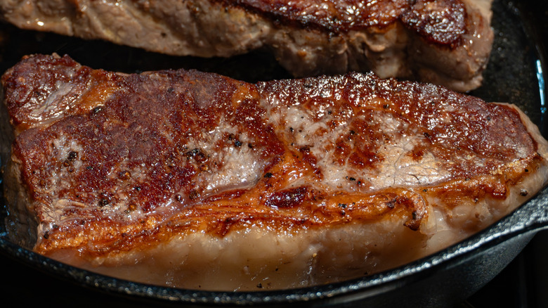 Primer plano de la reacción de Maillard en una tira de Nueva York en una sartén de hierro fundido