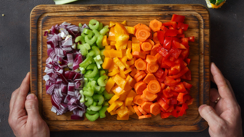 Manos sosteniendo una tabla para cortar de coloridas verduras picadas