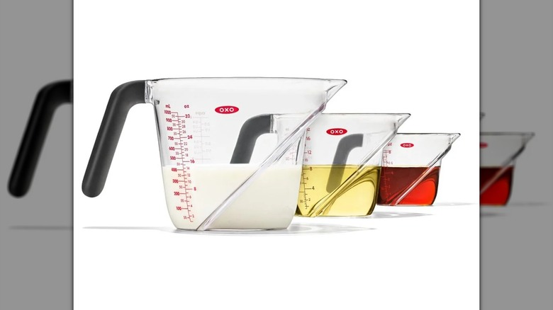 Juego de vasos medidores en ángulo de 3 piezas OXO Good Grips sobre un fondo blanco, todos llenos de líquidos de diferentes colores