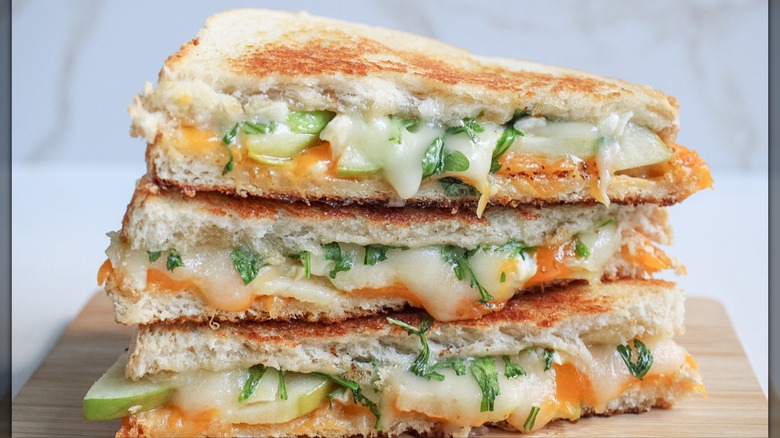 Tres trozos de queso cheddar asado con manzana apilados sobre una tabla de madera