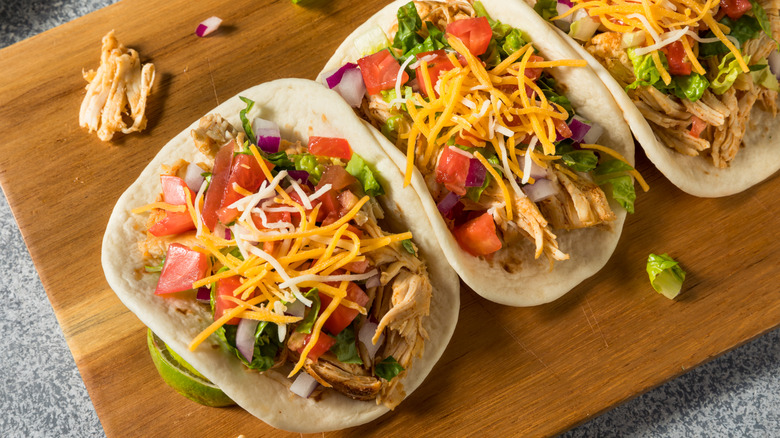 tres tacos de pollo sobre una tabla de cortar de madera