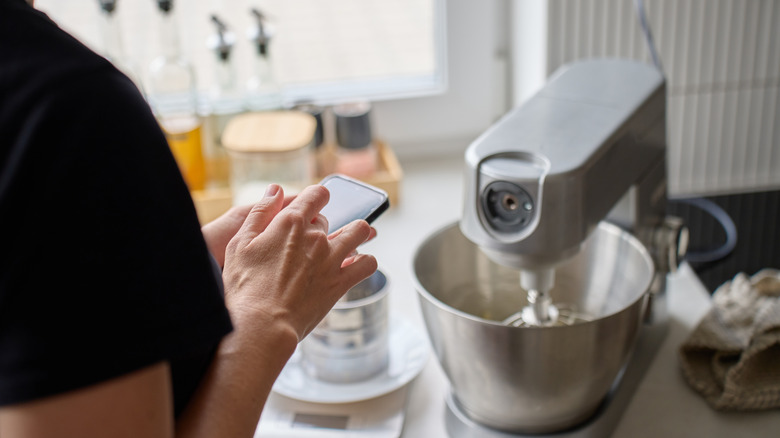 Una mujer revisa su teléfono mientras la batidora mezcla ingredientes