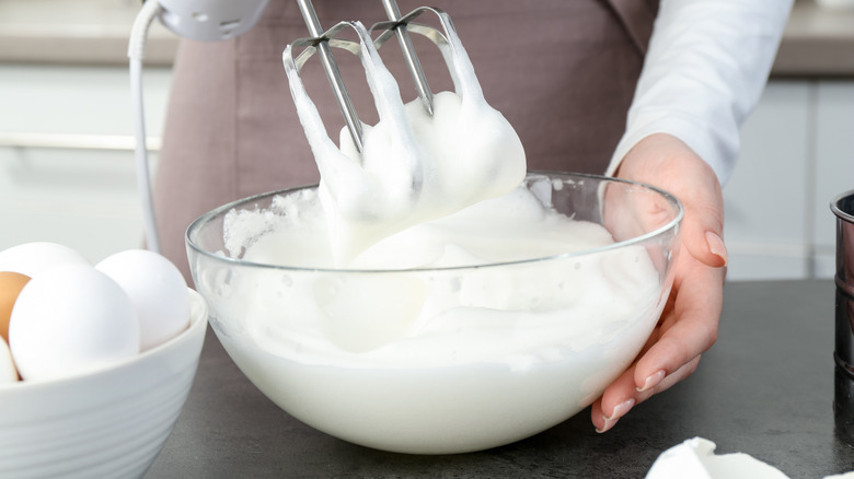 Una mujer con delantal bate claras de huevo con una batidora de mano