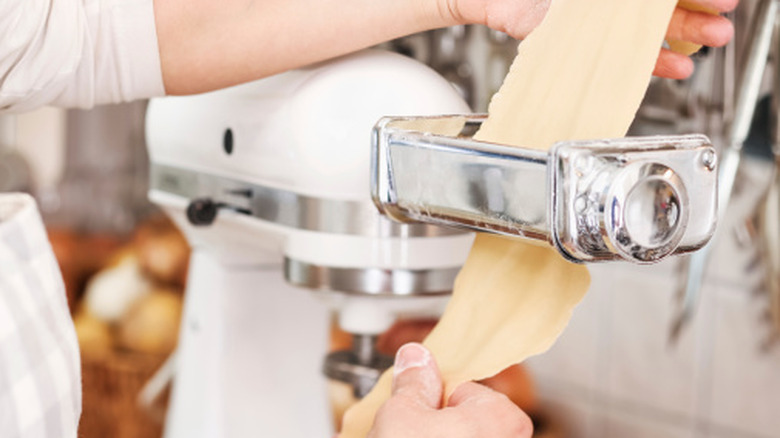 Un panadero enrolla la masa de pasta a través de un accesorio para pasta con batidora