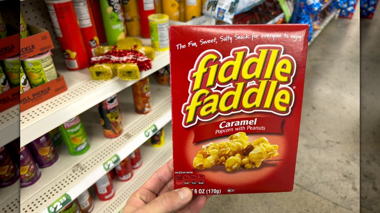 Una mano sosteniendo una caja de palomitas de maíz Fiddle Faddle Caramel en una tienda