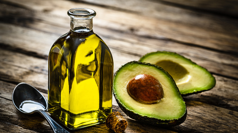 Aceite de aguacate en frasco de vidrio con cuchara y aguacates frescos cortados por la mitad