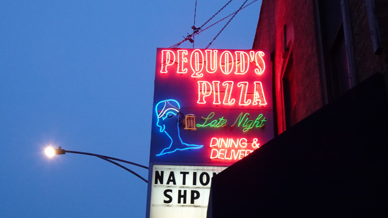 El exterior de Pequod's Pizza muestra un letrero de neón con el nombre del restaurante más "Cenas nocturnas y entrega a domicilio"