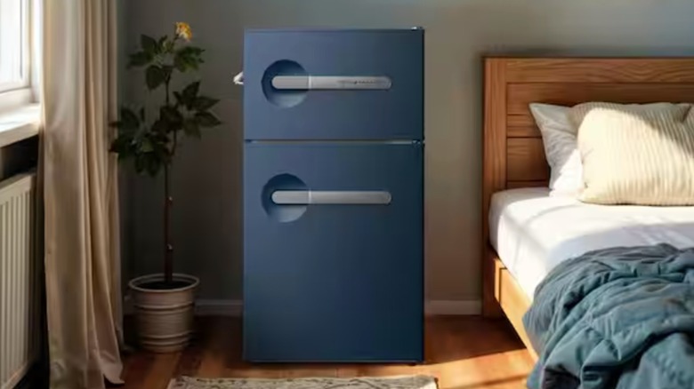 Un mini refrigerador Frigidaire de estilo vintage, de 2 puertas, de color azul oscuro, en un dormitorio.