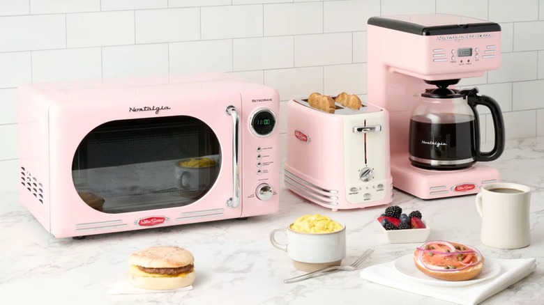 Un conjunto de electrodomésticos de cocina Nostalgia de estilo vintage en color rosa sobre un mostrador.