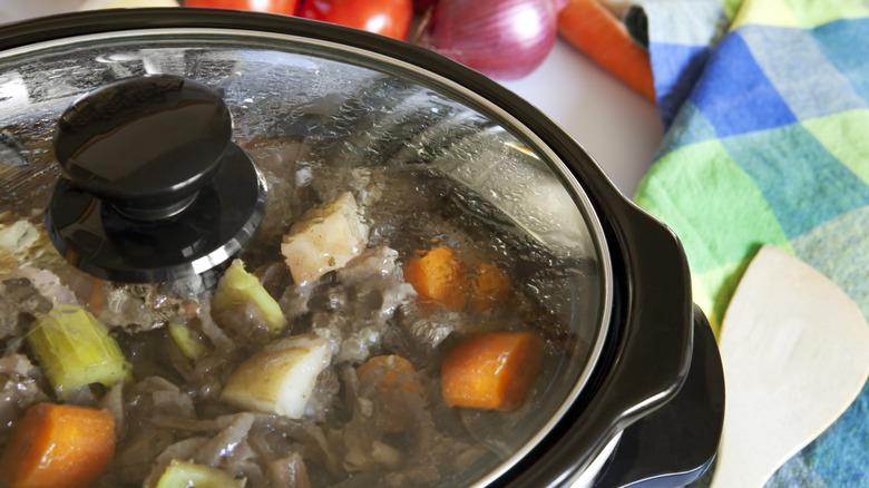 Primer plano de la tapa de una olla de barro con carne, zanahorias, patatas y apio visibles en el interior