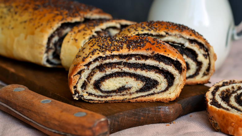 Un rollo de semillas de amapola y nueces en rodajas sobre una tabla de madera