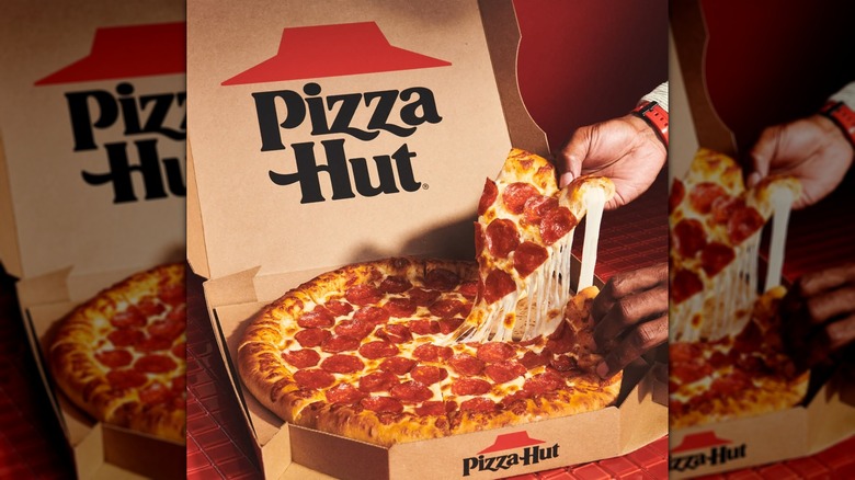 Una mano sacando una rebanada de pizza de pepperoni con queso de una caja de Pizza Hut